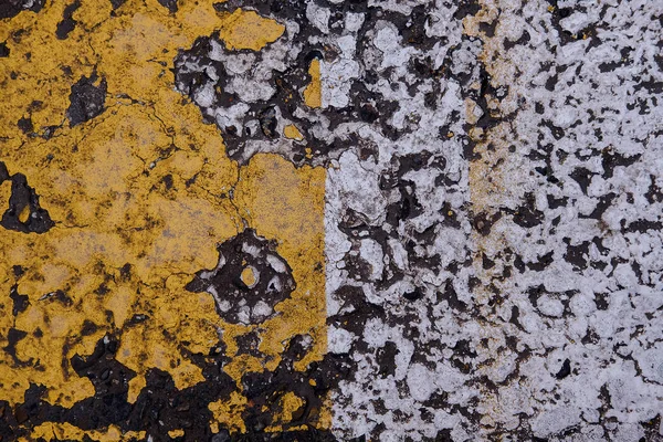 Peeling paint on asphalt and road markings. Asphalt crosswalk surface texture detail with peeling old white and yellow paint. Background