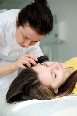 Kadın dermatolog cilt muayenesi yaparken profesyonel bir dermatoskop kullanarak, yüzünde benign benler kontrol. Dermatolog bir kadın hastada doğum lekeleri ve benler inceleyerek. Dermatoloji Kliniği