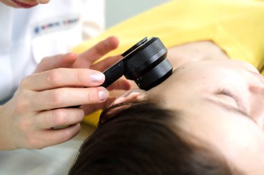 Kadın dermatolog cilt muayenesi yaparken profesyonel bir dermatoskop kullanarak, yüzünde benign benler kontrol. Dermatolog bir kadın hastada doğum lekeleri ve benler inceleyerek. Dermatoloji Kliniği