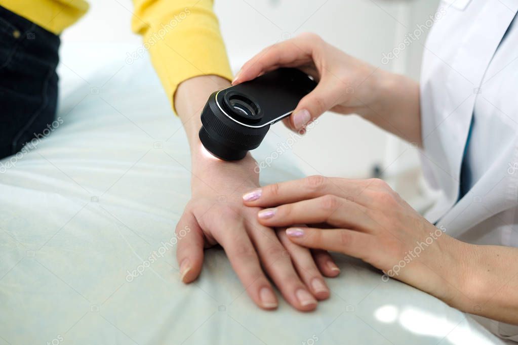 Female dermatologist using a professional dermatoscope while doing skin examination, Checking benign moles on hand. Dermatologist examining birthmarks and moles on a female patient. Dermatology Clinic