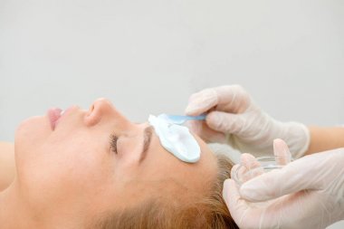 Yüz soyma maskesi, spa güzellik tedavisi, cilt bakımı. Spa salonunda güzellik uzmanı tarafından yüz bakımı yaptıran kadın. bir kız hastanın yüzüne krem maskesi uygulayan ometolog. Kozmetoloji. Yakın çekim