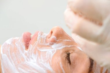 Yüz soyma maskesi, spa güzellik tedavisi, cilt bakımı. Spa salonunda güzellik uzmanı tarafından yüz bakımı yaptıran kadın. bir kız hastanın yüzüne krem maskesi uygulayan ometolog. Kozmetoloji. Yakın çekim