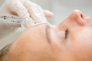 Mezoterapi yapan kozmetolog. Şırınga ve iğne, yüz kozmetik güzellik enjeksiyonu. Kadın hasta güzellik te yüz gençleştirme prosedürü alıyor. Hırdavat kozmetolojisi, Hyaluronik Asit.  