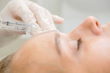 Mezoterapi yapan kozmetolog. Şırınga ve iğne, yüz kozmetik güzellik enjeksiyonu. Kadın hasta güzellik te yüz gençleştirme prosedürü alıyor. Hırdavat kozmetolojisi, Hyaluronik Asit.  