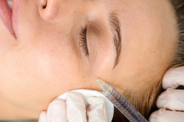 Mezoterapi yapan kozmetolog. Şırınga ve iğne, yüz kozmetik güzellik enjeksiyonu. Kadın hasta güzellik te yüz gençleştirme prosedürü alıyor. Hırdavat kozmetolojisi, Hyaluronik Asit.  