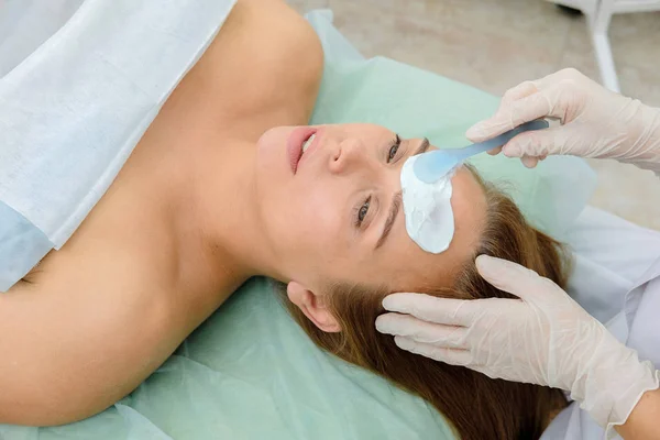 Face peeling mask, spa beauty treatment, skincare. Woman getting facial care by beautician at spa salon. osmetologist applying  cream mask on face of a girl patient. Cosmetology.  Close up