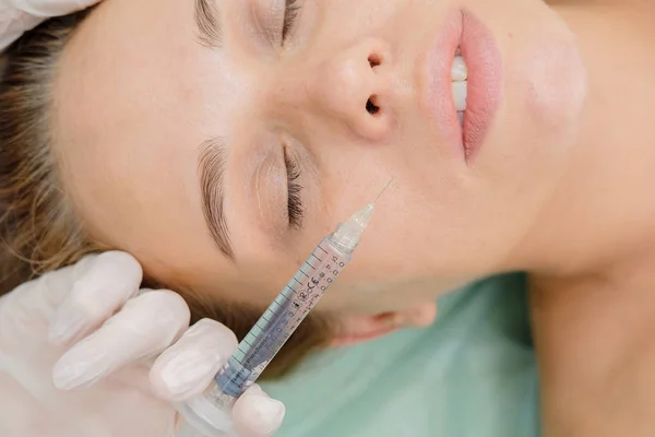 Cosmetologist making mesotherapy. Syringe and needle, facial cosmetic beauty injection. Woman patient is getting face rejuvenation procedure at beautician. Hardware cosmetology, Hyaluronic Acid.