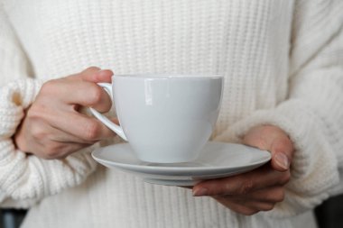 Beyaz örme kazaklı kadın bir fincan kahve tutuyor. Bir fincan çayla kadın elleri. Yakın çekim