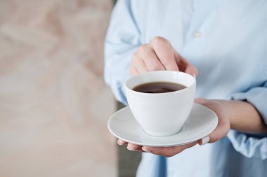 Bir fincan kahve tutan kadın. Bej arka planda siyah çay fincan ile Kadın elleri. Yakın çekim