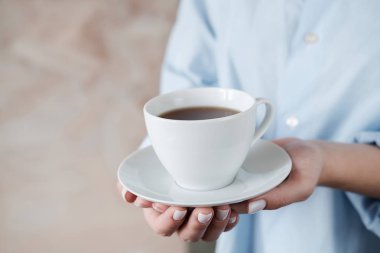 Bir fincan kahve tutan kadın. Bej arka planda siyah çay fincan ile Kadın elleri. Yakın çekim