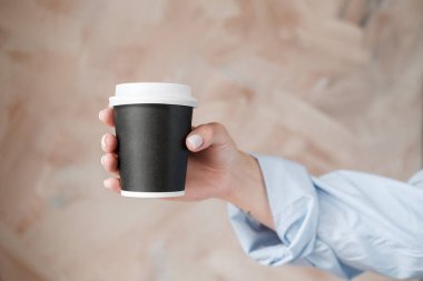 Mavi bluzgiymiş kadın elinde siyah bir fincan kahve tutuyor. Bej arka planda siyah çay fincan ile Kadın elleri. Yakın çekim