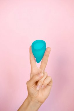 Kadın pembe arka plan üzerinde iki parmak mavi adet fincan tutarak. Dönem tampon yerine kadın hijyeni alternatif ürün. Adet, kritik günler, kadın dönemleri. Sıfır atık