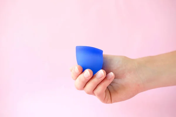 Woman holding in hands blue menstrual cup on pink background. Feminine hygiene alternative product instead of tampon during period. Menstruation, critical days, women periods. Zero waste, eco, ecology