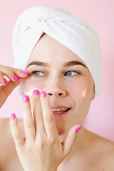 Young Woman with collagen pads under her eyes on pink background. Spa, skincare, beauty, cosmetics, wellness concept
