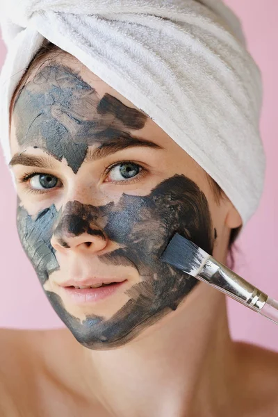 Young woman apply clay facial mask. Face peeling mask with charcoal, spa beauty treatment, skincare, cosmetology. Close up