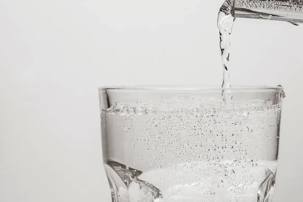 Pouring water from bottle into glass on white background