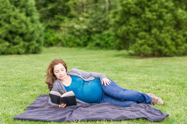 Wanita hamil sedang membaca buku di lapangan hijau di taman. — Stok Foto