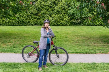 Parkta bisiklet süren hamile bir kadın telefonda konuşuyor..