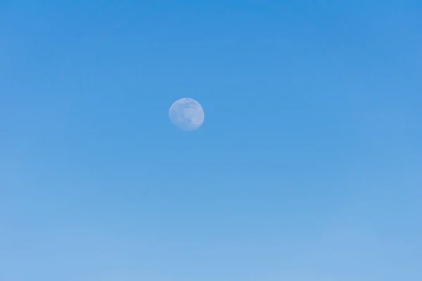 Ein kleiner Mond weit weg am blauen Himmel zur Abendzeit als Hintergrund. — Stockfoto