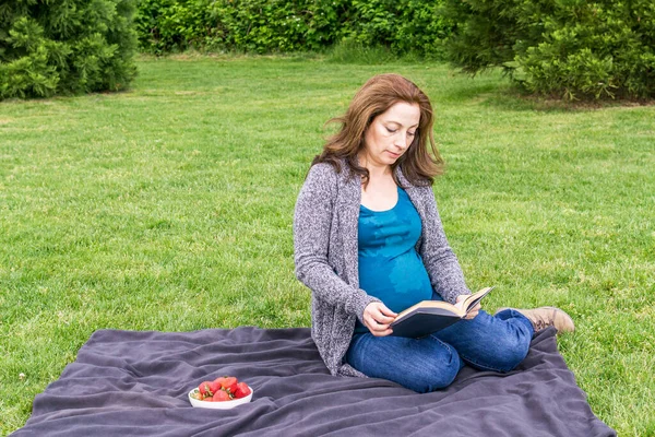 Wanita hamil sedang membaca buku di lapangan hijau di taman. — Stok Foto