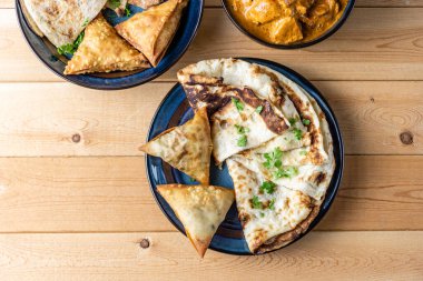 Hint atıştırmalıkları samosa sarımsaklı ekmek tereyağlı tavuk ahşap masada.