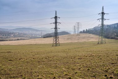 Ulusal parktaki tarımsal arazi ve otlaklardaki eski elektrik şebekesi aktarım kuleleri. Çayır dağlarında mavi gökyüzünün altında paslı yüksek voltajlı elektrik direkleri. Litomerice, Çek Cumhuriyeti, Avrupa.