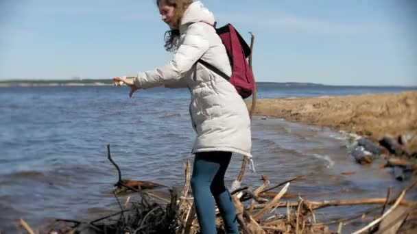 Schöne junge Frau, die am Ufer des Flusses entlang geht und trockene Äste sammelt — Stockvideo