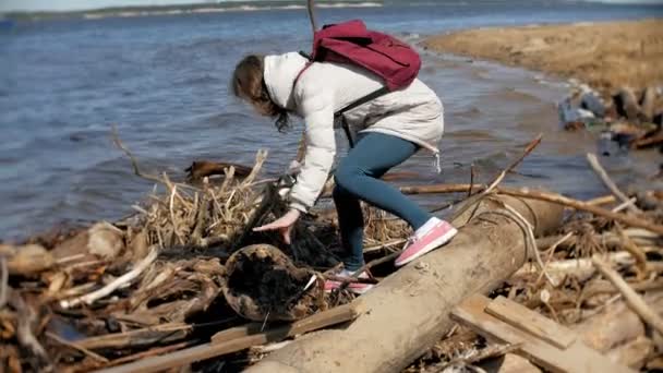 Красивая молодая женщина, идущая вдоль берега реки и собирающая сухие ветви — стоковое видео