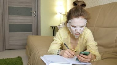 Genç kadının temizlik maskesi, yüz maskesi maskesi yapması tıklama ile smartphone evde kanepede