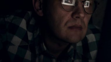 Gözlüklü bir adam gece geç saatlerde çalışıyor. Önünde bir yakın çekim bilgisayar ekranında gördüğü endişeli görünüyor,