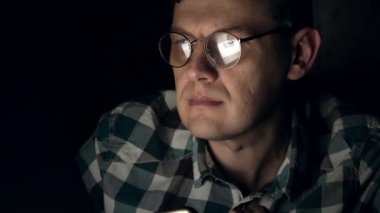 Gözlüklü bir adam gece geç saatlerde çalışıyor. Önünde bir yakın çekim bilgisayar ekranında gördüğü endişeli görünüyor,