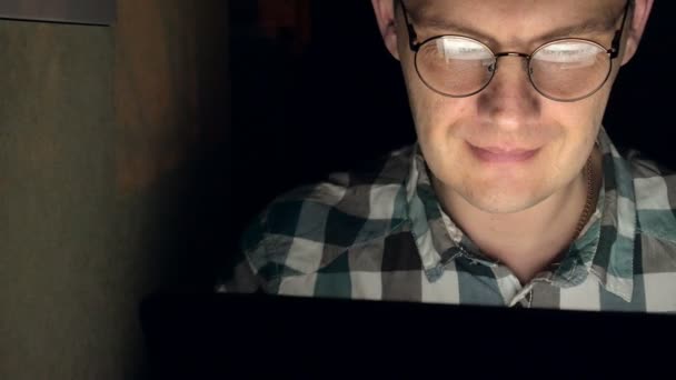 Egy férfi szemüveg működik, késő este. Úgy néz ki, zaklató, látja a számítógép képernyőjén, előtte, egy közeli — Stock videók