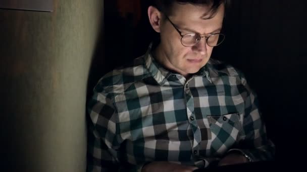 Un hombre con gafas trabaja hasta tarde por la noche. Se ve preocupado, ve en la pantalla de la computadora frente a él, un primer plano — Vídeo de stock