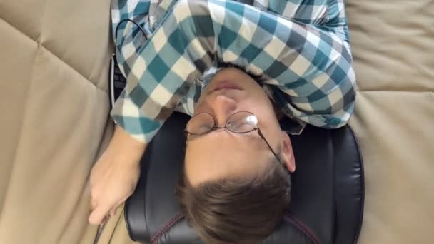 Man lies on the couch at home, under the head of a massager, relaxed state — Stock Video