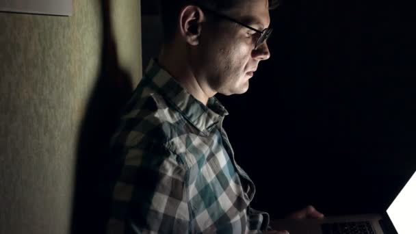 Człowiek w okularach działa późno w nocy. Wygląda on martwi się, on widzi na ekranie komputera przed nim, zbliżenie — Wideo stockowe