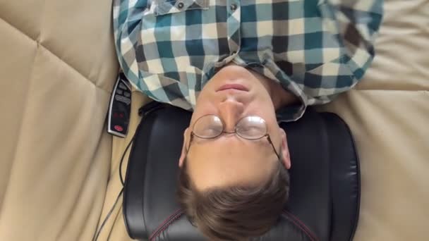 Mann liegt zu Hause auf der Couch, unter dem Kopf eines Massagegeräts, entspannter Zustand — Stockvideo