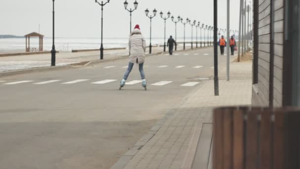 Ung vacker kvinna i en röd hatt, bär sportig varma kläder och valsar, ridning på vägen på kusten — Stockvideo