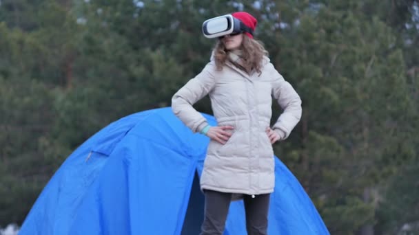 Atractiva joven turista con sombrero rojo se sienta en una carpa turística y disfruta de un casco de realidad virtual — Vídeos de Stock