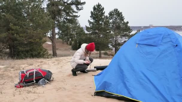Vonzó fiatal turista nő egy piros kalap gyűjt egy turisztikai sátorban, az erdő közelében a tengerparton — Stock videók