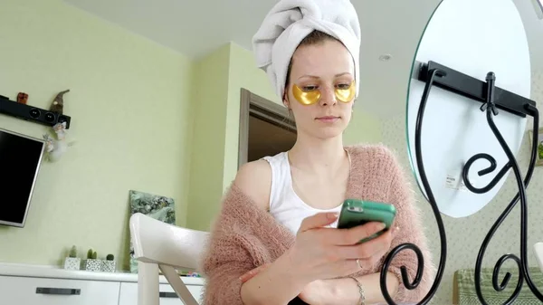 Attraente donna d'affari che applica macchie facciali cosmetiche a casa, parlando al telefono — Foto Stock
