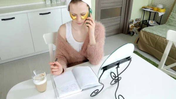 Приваблива ділова жінка застосовує косметичні плями обличчя вдома, розмовляючи по телефону — стокове фото