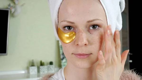 Mujer atractiva espiando parches faciales cosméticos en casa — Foto de Stock