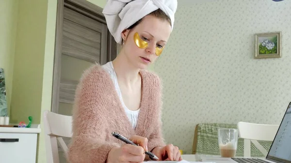 Привлекательная деловая женщина, применяющая косметические пятна на лице дома, работающая за ноутбуком — стоковое фото