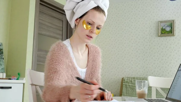 Привлекательная деловая женщина, применяющая косметические пятна на лице дома, работающая за ноутбуком — стоковое фото
