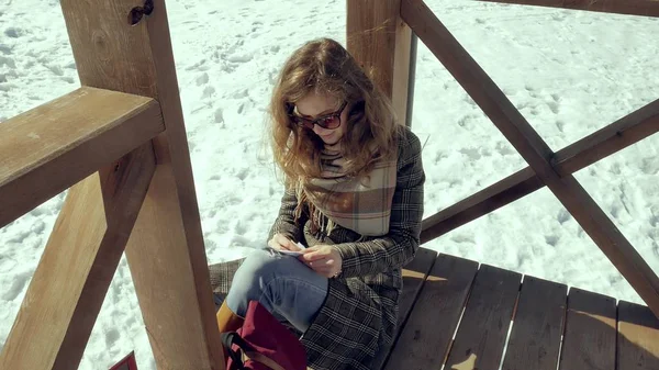 En ung kvinna sitter på en trä veranda, tyst röra origami papper planet med fingrarna och sätta den på knä. Flickan sitter utomhus med vita aerogamy flygplan, Stäng vy, — Stockfoto