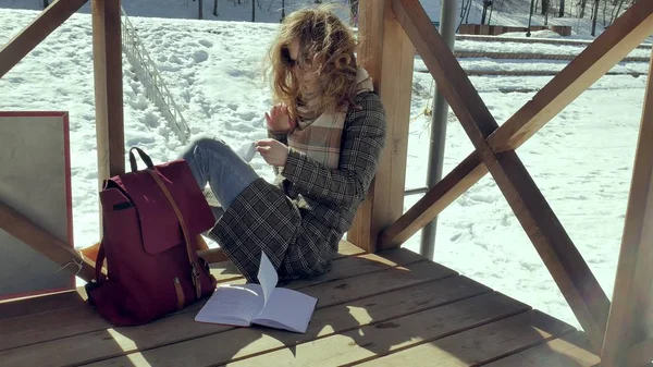 En ung kvinna sitter på en trä veranda, tyst röra origami papper planet med fingrarna och sätta den på knä. Flickan sitter utomhus med vita aerogamy flygplan, Stäng vy, — Stockfoto