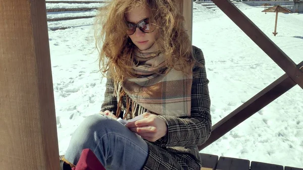 Una joven se sienta en una veranda de madera, tocando silenciosamente el avión de papel de origami con los dedos y poniéndolo de rodillas. Chica sentada al aire libre con aviones de aerogamia blanca, vista cercana , — Foto de Stock