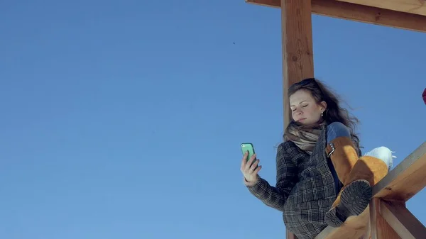 Kvinna med Smartphone slappnar på bänken i vacker Park. Ung kvinna att göra gester på telefonens Display. Teknik utomhus — Stockfoto