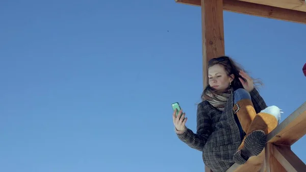 Kvinna med Smartphone slappnar på bänken i vacker Park. Ung kvinna att göra gester på telefonens Display. Teknik utomhus — Stockfoto