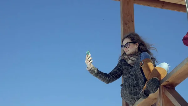 Γυναίκα με τη χρήση Smartphone χαλαρώνει στον πάγκο στο όμορφο πάρκο. Νεαρή γυναίκα στο κάνοντας χειρονομίες στην οθόνη του τηλεφώνου. Τεχνολογίας σε εξωτερικούς χώρους — Φωτογραφία Αρχείου